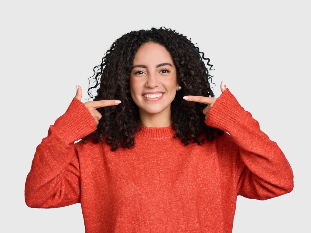 Smiling woman pointing at her white, healthy teeth after a teeth cleaning at 608 Family Dental in Sun Prairie, WI.